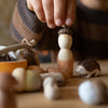 Child's hand interacting with a wooden acorn figurine on a table with other small objects.