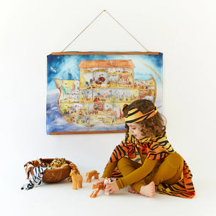 Child in a tiger costume playing with toys in front of a colorful Noah's Ark poster.
