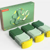 Set of green, gray, and yellow geometric building blocks with packaging in the background.