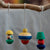 Three colorful wooden hanging ornaments with painted geometric shapes suspended from a natural wood branch against a soft blurred gray background.