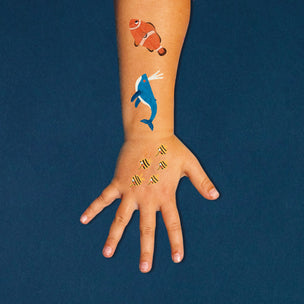 Hand with temporary tattoos of a whale, fish, and goldfish on a blue background