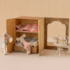 Miniature dollhouse with open wooden wardrobe, plush toys, and small table with chair on a beige background.