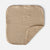 A square muslin baby blanket in a warm beige color with a subtle woven grid pattern, shown on a light gray background with one corner folded over to reveal the soft fleece backing.