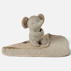 A beige plush elephant toy sitting on a matching patterned fabric blanket against a clean white background.
