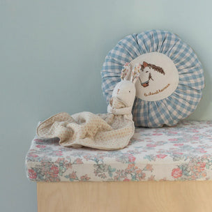 Floral-patterned bench with a plush Maileg toy and decorative pillow against a light blue wall.