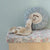 Floral-patterned bench with a plush Maileg toy and decorative pillow against a light blue wall.