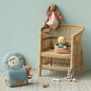 Wicker children's chair with Maileg toys against a light green wall