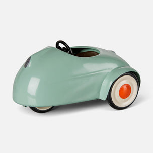 A retro-style pedal toy car in a glossy mint green color, featuring cream-colored wheels with orange centers and a black steering wheel, shown on a light gray background.