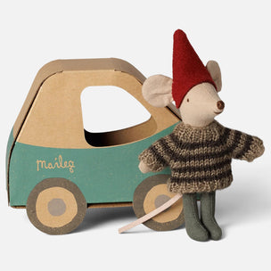 A Maileg brand plush mouse toy dressed as a gnome, standing next to a wooden toy car. The mouse has a red felt hat, a brown and beige striped knit sweater, and green pants, holding a light pink string.