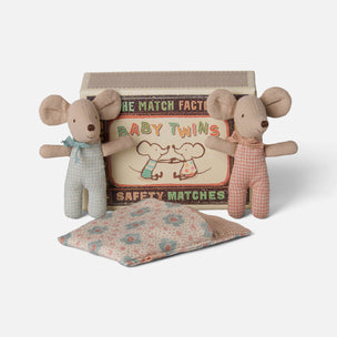 A baby toy set featuring two plush mouse dolls, one in light blue and one in pink gingham, standing in front of a wooden box labeled 'The Match Factory Baby Twins Safety Matches', with a matching floral cushion in front on a light gray background.