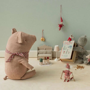 A styled collection of plush toys and miniature accessories arranged on a light wood floor against a pale green wall. The set includes a large pinkish-beige pig plush wearing a red-and-white gingham scarf, a gray mouse plush, a small red-and-white dressed doll, a miniature lamp, chair, and framed picture, plus tiny scattered gold coins.