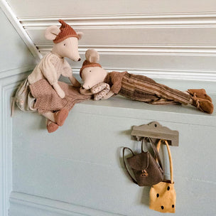 A cozy nursery-style scene with two plush stuffed mice posed on a white paneled ledge. One mouse wears a cream sweater and brown hat, while the other wears striped pajamas.