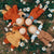 Four handmade fabric dolls with long yarn hair are arranged in a circle on a grassy ground with white daisies. The dolls are dressed in warm autumn colors including rust orange, mustard yellow, brown, and light blue.