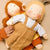 Two handmade fabric dolls posed together on a soft beige background. The doll in front has curly blonde yarn hair, blue embroidered eyes, and wears a light blue shirt with tan overalls.