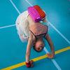 Person performing a handstand on a blue floor with colorful equipment.