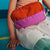 Child wearing a colorful backpack with an orange front and pink sides, sitting on a blue floor.