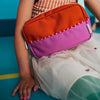 Child wearing a colorful backpack with an orange front and pink sides, sitting on a blue floor.