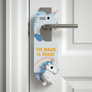 A white cardboard do-not-disturb door hanger with a unicorn design and the text 'THE MAGIC IS READY' hangs from a silver metal door handle on a white paneled door.