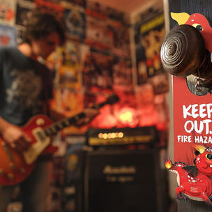 Person playing guitar in a room with posters and a Eugy door hanger 'Keep Out, Fire Hazard' sign.