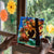 Person holding a colorful tree painting with a bear silhouette in front of a window with decorative flowers.
