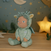 Plush toy dressed as a dragon on a wooden surface with a starry background