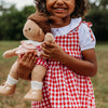 Child in a red and white checkered dress holding a doll outdoors.