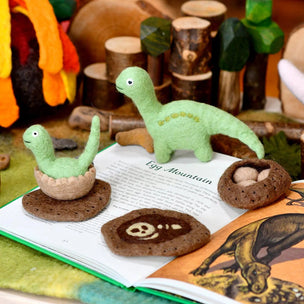Plush dinosaur toys on an open book with a toy forest in the background