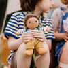Child holding a small doll with a striped shirt and yellow pants, sitting outdoors.