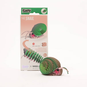 A 3D cardboard snail model toy next to its retail packaging box. The toy features a green spiral shell and a pinkish-brown body with a small antennae.