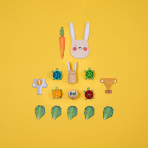 Set of wooden toys including a rabbit head, carrots, turtles, and leaves on a yellow background