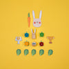 Set of wooden toys including a rabbit head, carrots, turtles, and leaves on a yellow background
