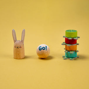 Wooden toy rabbit, ball with 'Go!' text, and stack of colorful rings on a yellow background