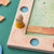 Close-up of a wooden board game with a small wooden player standing in a yellow slot, surrounded by colorful game pieces on a green surface.