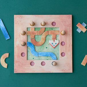 A square wooden puzzle board with a pastel landscape design, surrounded by scattered wooden puzzle pieces on a dark green background.