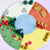 A circular felt craft rug or play mat featuring four colored quadrants: white, orange, yellow, and green, with small felt trees, mushrooms, flowers, leaves, and stars attached around the border.