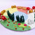 A colorful felt garden play mat with red and white mushrooms, green grass, pink flowers, and a pastel background of yellow, pink, blue, and white sections on a light purple surface.
