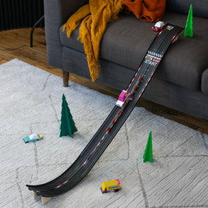 Toy race track set up on a carpeted floor with toy cars and trees.