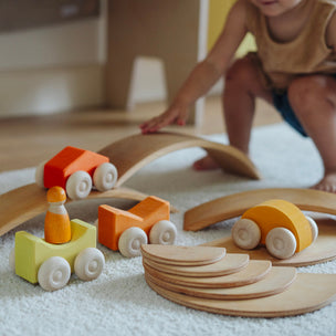 Children's wooden toy car set on a blanket with a child playing in the background.