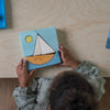 Child playing with a wooden sailboat puzzle on a wooden table