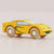 A small wooden toy sports car in bright yellow with black graphic decals, a light blue windshield, and natural wood wheels, photographed on a plain light background.