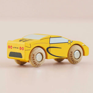 A yellow wooden toy sports car with hand-painted black and light blue details, photographed on a soft beige background.