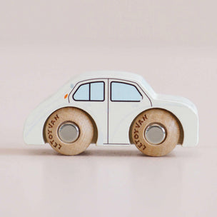 A small wooden toy car with a white body and natural wood wheels, photographed on a plain light beige background.