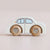 A small wooden toy car with a white body and natural wood wheels, photographed on a plain light beige background.
