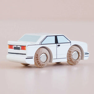 Wooden toy car with white body and black details on a beige background