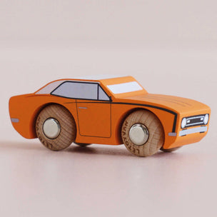 An orange wooden toy car with hand-painted details, including black outlines, white accents, and textured brown wheels, shown on a neutral beige background.