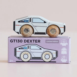 A wooden toy car labeled 'LET'S PLAY' sits on top of its lavender packaging box, which reads 'GT130 DEXTER' and 'Limited Edition'. The toy car is white with light brown wooden wheels and small blue and orange details.
