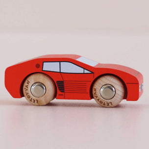Red toy car with wooden wheels on a light pink background