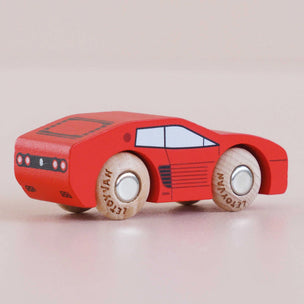 Red toy car with wooden wheels on a light pink background