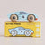 A light blue wooden toy race car with the number 6 sits on top of its yellow 'GT145 FRED' packaging box. The box features an illustration of the same car and small eco-style icons on the right side.