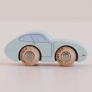 A light blue wooden toy car with natural wood wheels, photographed on a plain beige background.